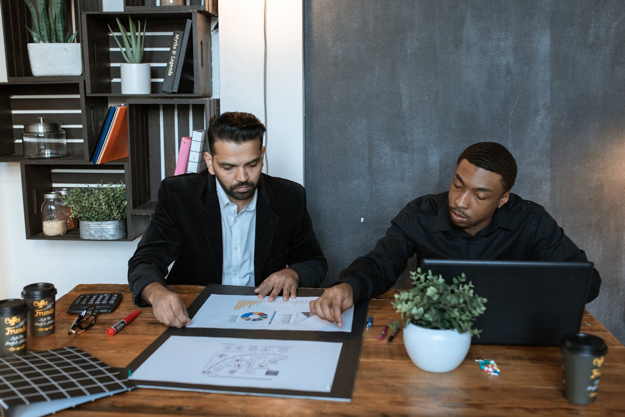 Two men at a table, analysing bankruptcy information with a laptop and various papers in front of them.